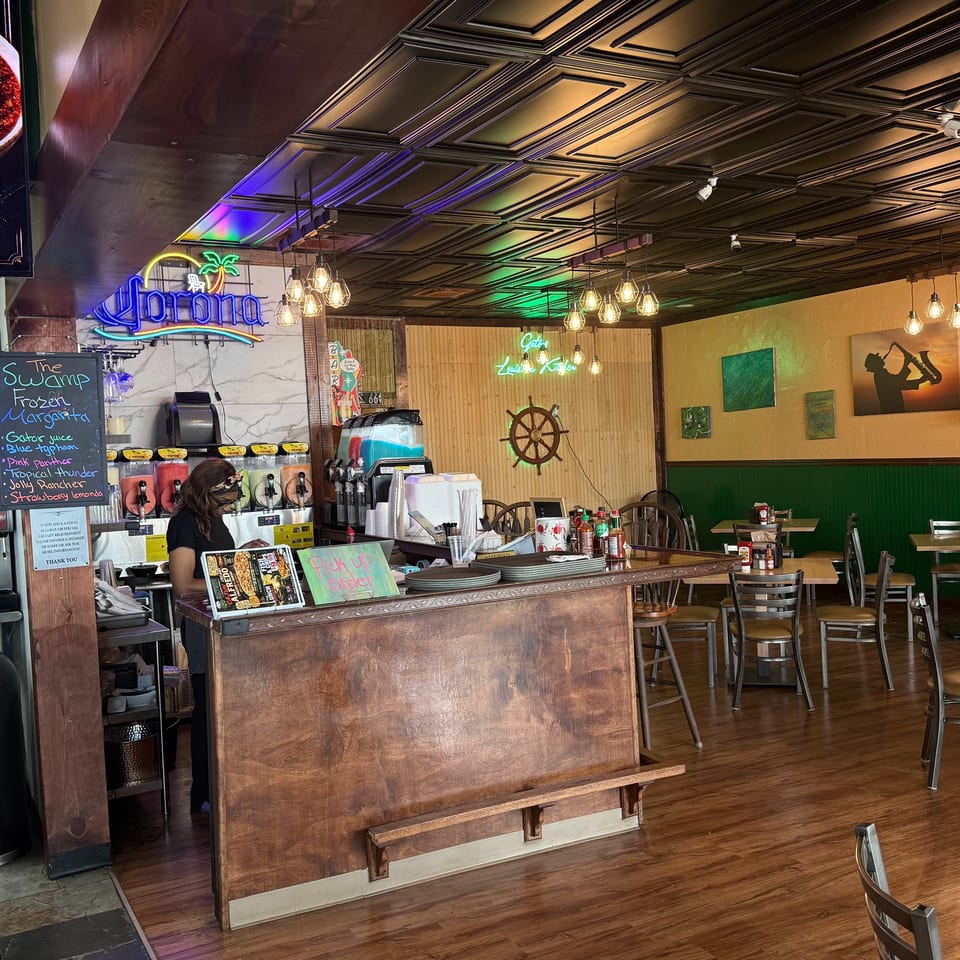 A restaurant interior with a wooden counter, margarita machines, and a woman standing behind the counter.