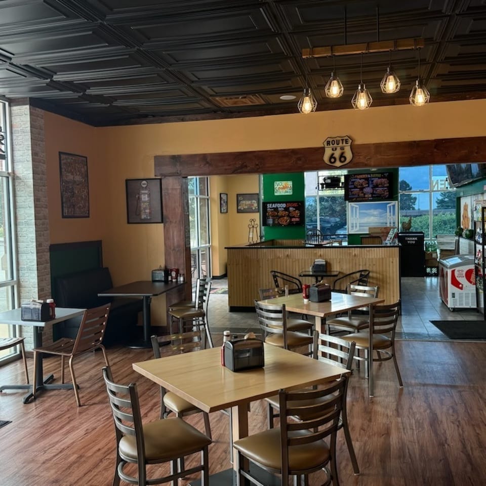 Empty restaurant interior with wooden tables, chairs, and a counter with menu boards.