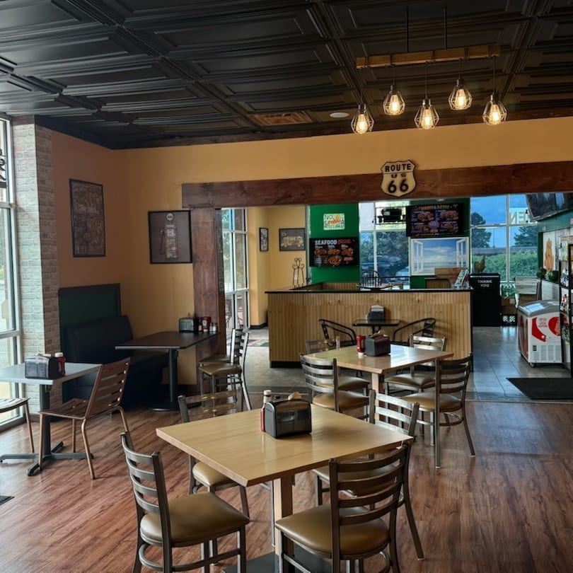 Empty restaurant interior with wooden tables, chairs, and a counter with menu boards.