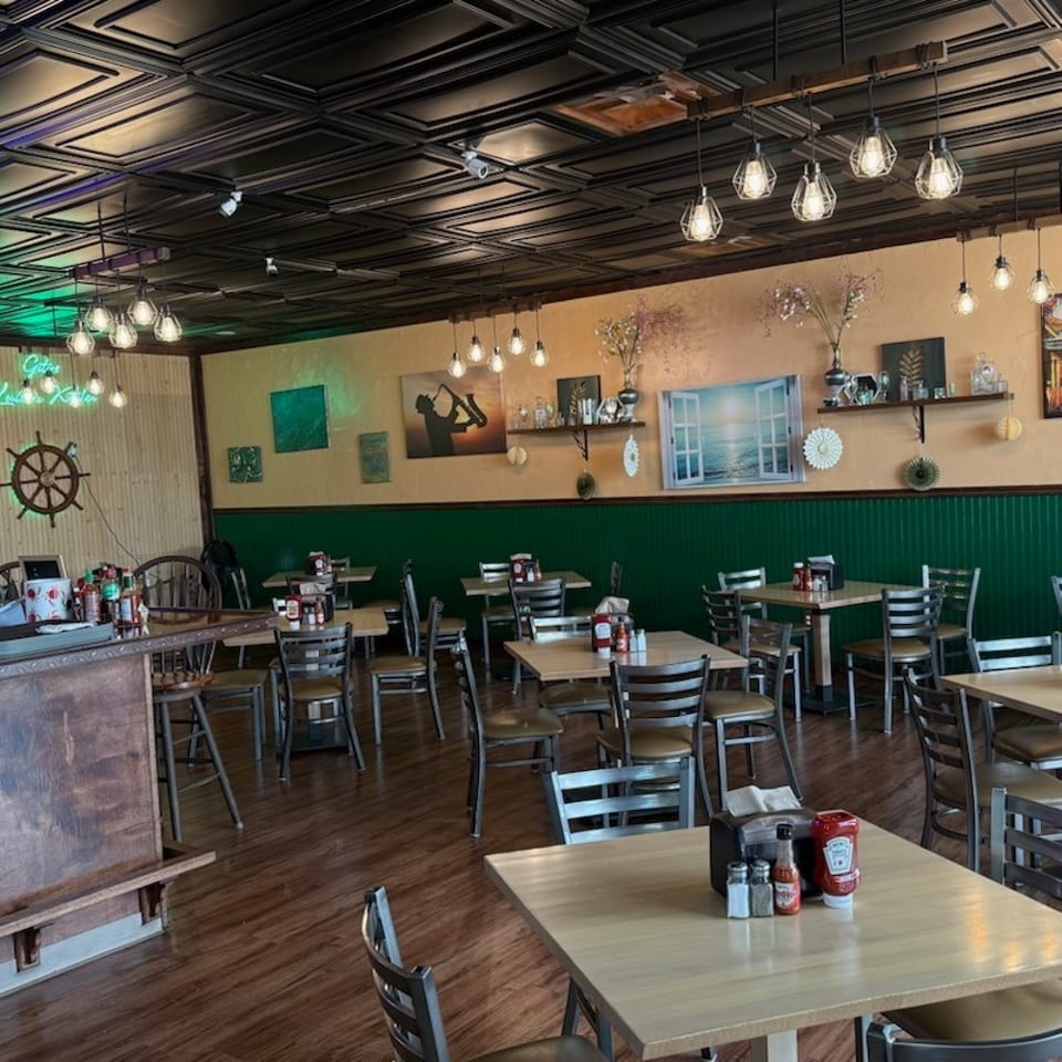 Empty restaurant dining room with wooden tables, chairs, and nautical-themed decor.